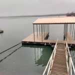 Covered boat dock with metal roof and central walkway on calm Grand Lake water