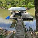 Covered boat dock with a wooden walkway and metal handrails leading to a floating platform on Grand Lake in Oklahoma