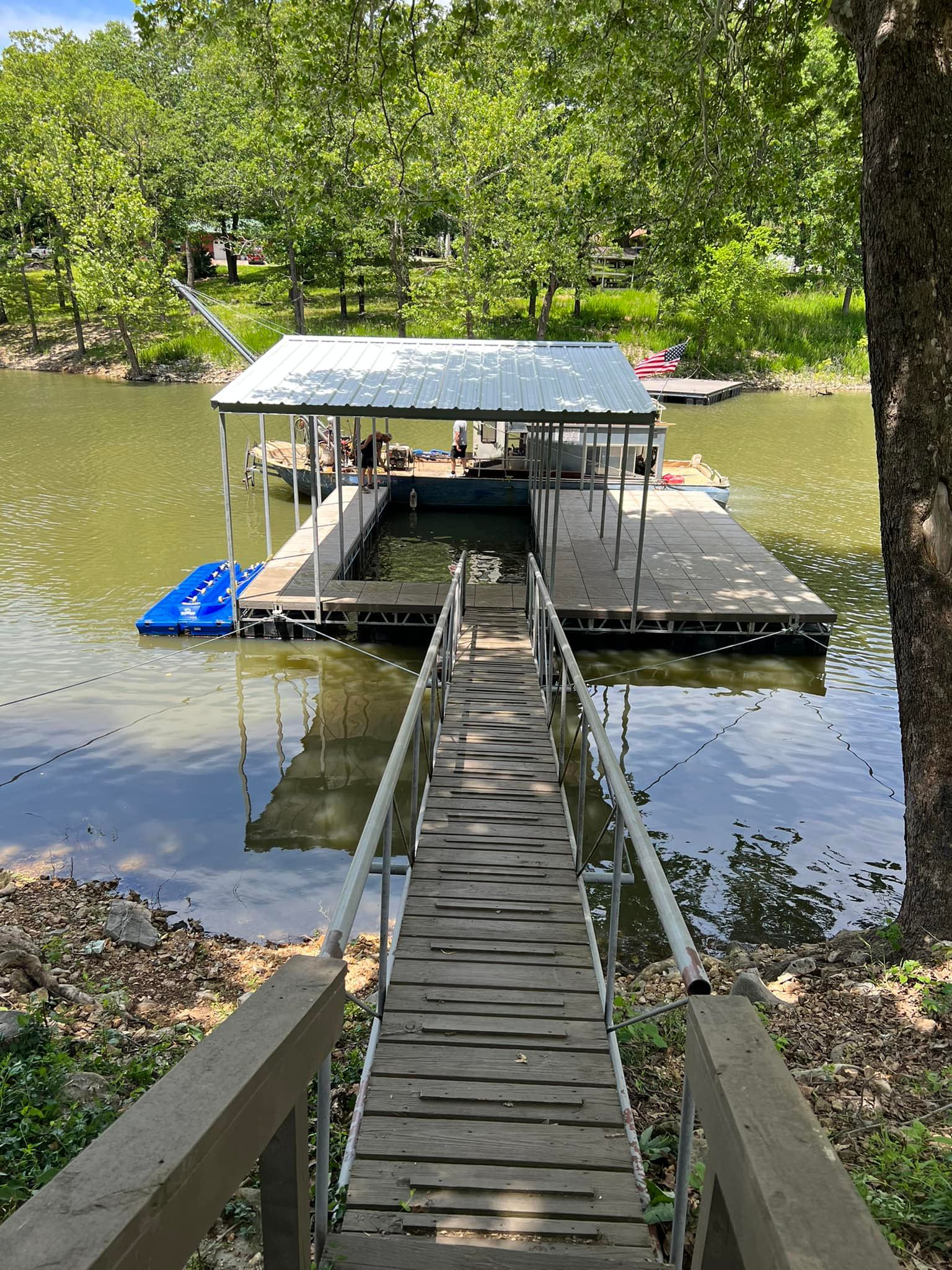 Covered boat dock with a wooden walkway and metal handrails leading to a floating platform on Grand Lake in Oklahoma
