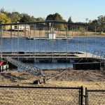 Covered boat dock under construction on Grand Lake Oklahoma with metal framing, floating platform, and boat lift access at a lakefront property