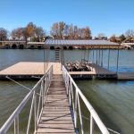 Covered boat dock with a wooden walkway, metal railings, and boat lift slips on Grand Lake in Grand Lake, Oklahoma
