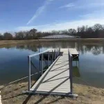 Wooden boat dock walkway with metal railings extending into calm Grand Lake water with a floating dock section and shoreline view